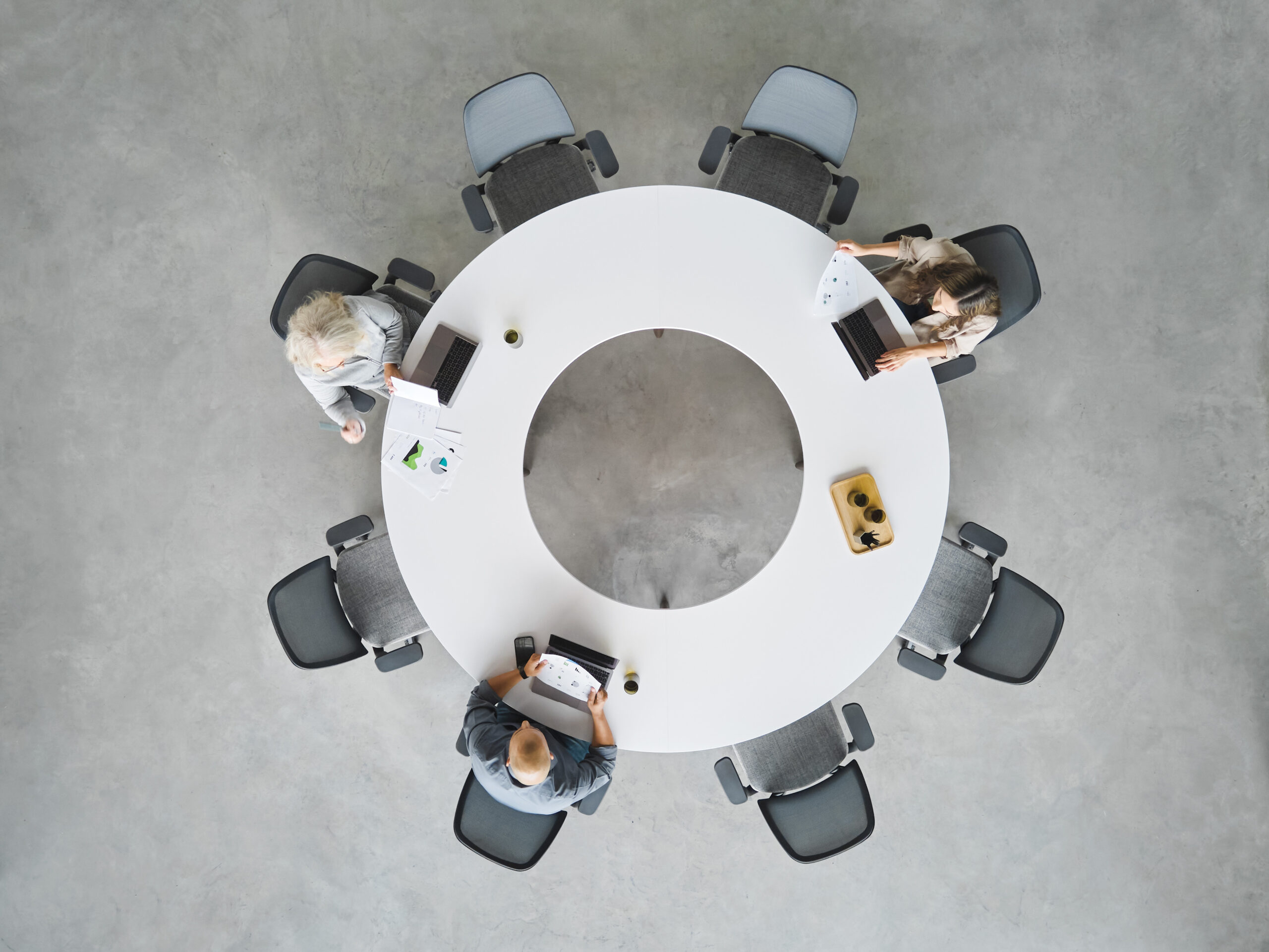 birds eye view of a circular table with three people sitting at it on their laptops