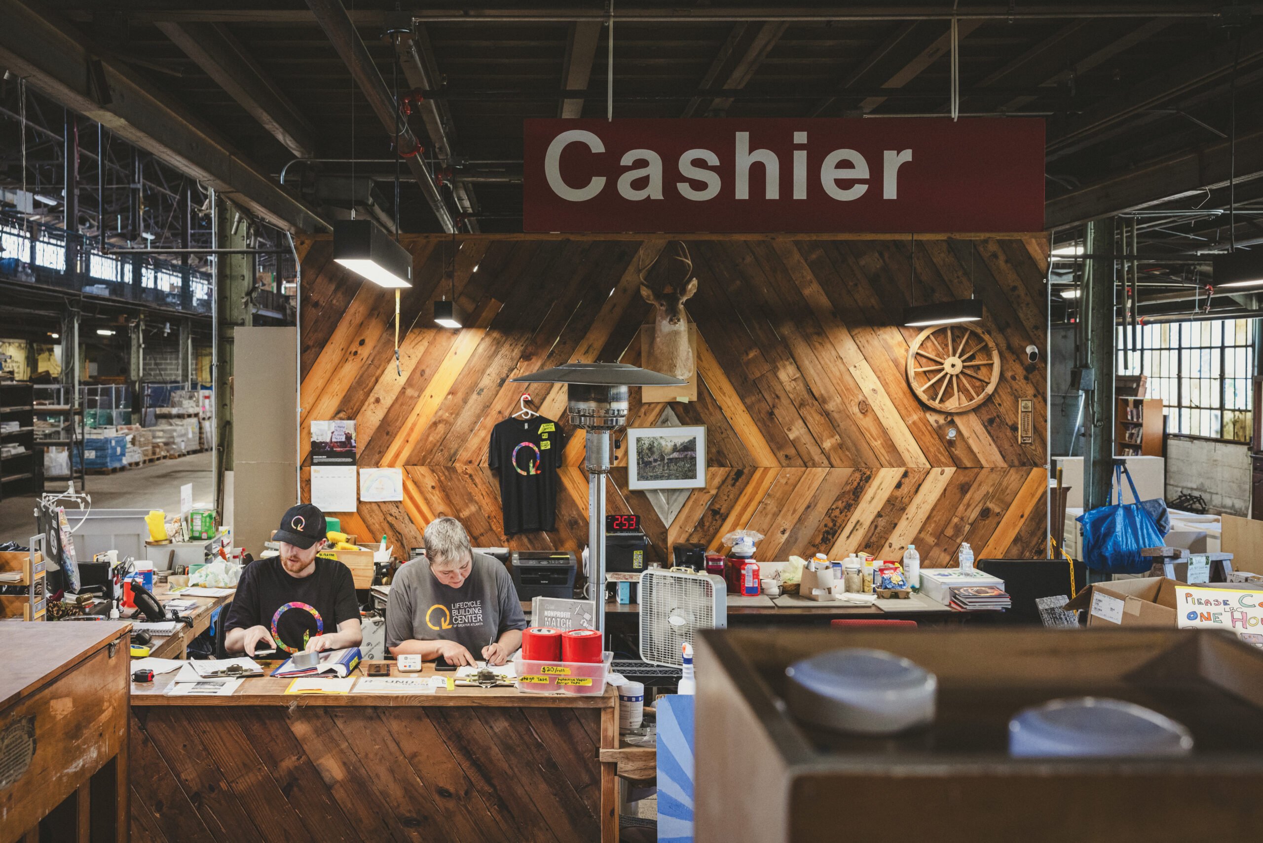two people sitting at a front desk within a warehouse with a big sign that says cashier