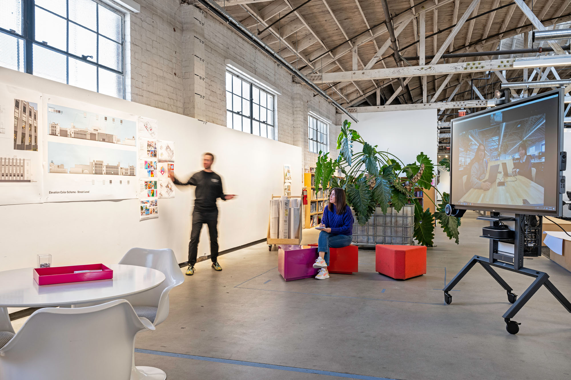 interior of workplace with a person at a whiteboard and others joining on video chat