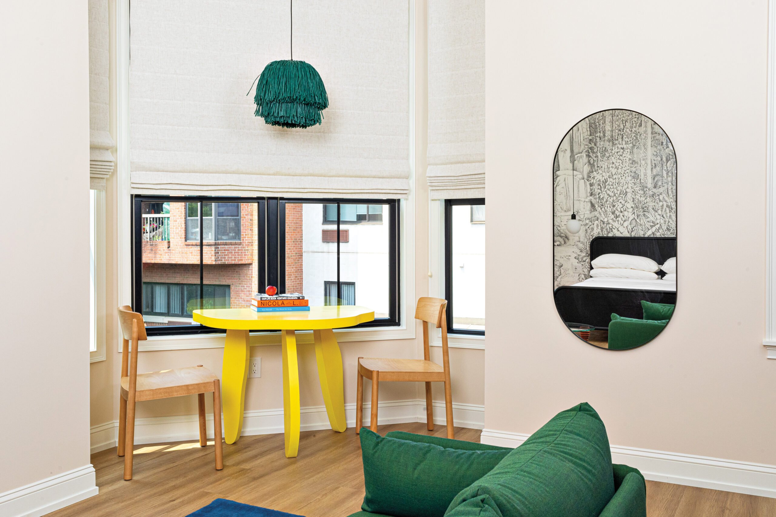 A yellow table next to a bay window with a green fringed light hanging above it
